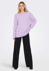 Jasnofioletowy, oversize'owy sweter z prążkowanym dekoltem i mankietami, zestawiony z czarnymi, szerokimi spodniami z wysokim stanem. Gładka faktura, luźny fason.