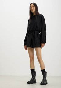 Top nero a maniche lunghe con vita arricciata, abbinato a pantaloni corti neri e stivali alla caviglia neri. Tessuto morbido con una vestibilità comoda.