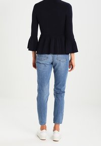 Marinblå ribbad stickad topp med utsvängda ärmar och peplumslut, kombinerad med ljusblå slim fit-jeans och vita sneakers. Minimalistisk design.