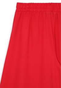 Pantalon à taille élastique rouge en matériau doux. Dispose d'une texture lisse et d'une coupe ample, idéal pour le confort et la liberté de mouvement.