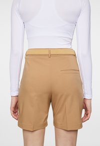 Beiga shorts med en slät textur, med ett smalt midjeband, en bakficka och en avslutning som når mitten av låret.