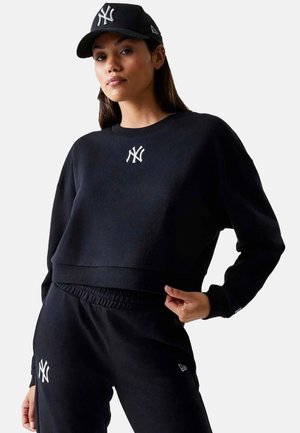 Zwarte cropped sweater met wit NY-logo, gecombineerd met bijpassende joggingsbroek. Zacht materiaal, geribde manchetten en tailleband, voor een relaxte pasvorm.