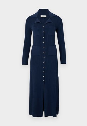 Robe tricotée bleu marine avec un col, des boutons sur le devant et deux poches poitrine. Présente une texture en côtes verticales et une fente à l'avant pour faciliter le mouvement.