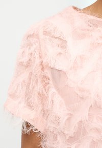 Απαλό ροζ διάφανο ύφασμα με στρωματοποιημένα, αέρινα φτερωτά κρόσσια σε ρούχο με κοντά μανίκια, που δείχνει μέρος του ώμου και του λαιμού.