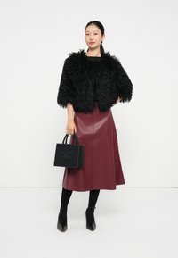 Giacca cropped in faux fur nera sopra una maglietta nera, abbinata a una gonna in faux leather bordeaux. Porta una piccola borsetta nera con dettagli borchiati.