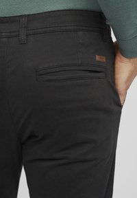 Zwarte broek van gladde stof, met een achterzak met een subtiel horizontaal ontwerp en een klein bruin leren logolabel genaaid.