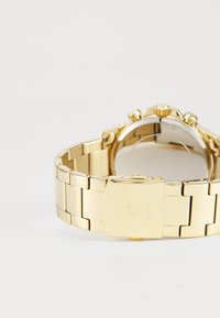 Montre-bracelet en métal doré avec un bracelet à maillons, dotée d'un boîtier rond, d'un cadran texturé, et d'une couronne et de poussoirs proéminents. Fermoir à l'arrière.