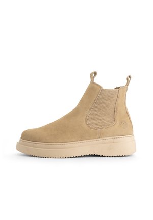 Beige suède Chelsea-boot met geprofileerde elastische zijpanelen, trekflappen op de enkel en een dikke geribbelde zool, zijwaarts weergegeven op een witte achtergrond.