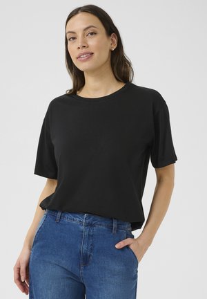 Sort kortærmet t-shirt, rund hals, blødt bomuldsstof, afslappet fit. Parret med blå jeans, hænderne i lommerne, minimalistisk design.
