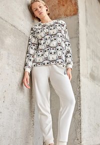 Sudadera blanca con un patrón de búhos, puños acanalados; combinada con pantalones deportivos crema que tienen un detalle cerca de la cadera. Tela suave y cómoda.
