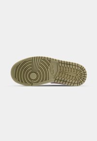 Semelle d'une basket Nike marron clair avec des motifs de crampons circulaires et rectangulaires et le logo Nike au centre sur fond blanc uni.