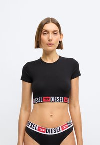 Svart kortermet crop topp med en bred elastisk kant med "DIESEL"-logoen i rødt og hvitt. Glatt, stretch stoff med en tettsittende form.
