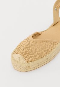 Espadrillas beige con toma intrecciata, suola in iuta contrastante e punta arrotondata. Presentano una fascia con anello per una vestibilità sicura.