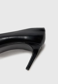 Scarpa nera in pelle con tacco alto e punta affusolata, texture liscia e tacco sottile a stiletto. Design minimalista senza hardware visibile.