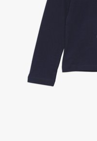 Pitkähihainen paita tummansinisestä puuvillasta, jossa on röyhelötekstuuri, suorat helmavarusteet ja klassinen pyöreä kaula-aukko.