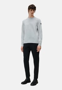 Lichtgrijze gebreide trui met een ronde hals en geribbelde zoom, gecombineerd met zwarte taps toelopende broek en zwarte enkellaarsjes.