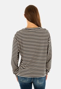 Lange mouwen shirt in zwart en crèmekleurige strepen. Zachte stof met een relaxte pasvorm, ronde hals en manchetten, gecombineerd met blauwe jeans.