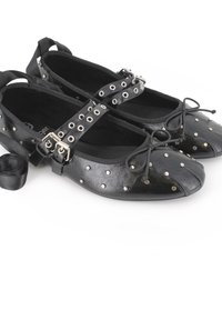 Bailarinas negras con superficie de cuero suave, adornadas con acentos de tachuelas plateadas, un detalle de lazo en la puntera y correas ajustables en el tobillo.