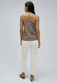 Haut sans manches en imprimé léopard avec des fines bretelles, en tissu lisse. Associé à un pantalon blanc à jambes droites et des sandales à talons noires.