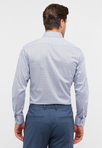 Camicia a maniche lunghe a fantasia blu con motivi circolari; tessuto liscio e colletto classico. Abbinata a pantaloni su misura.