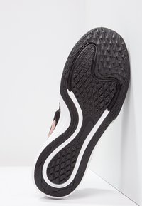 Musta urheilujalkineen pohja, jossa on teksturoitu kuvio, valkoisia kumikoristeita ja vaaleanpunainen paneeli sivussa. Pinnan kuviointi tarjoaa hyvän pidon.