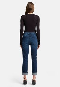 Jeans in denim blu scuro con una leggera affusolatura, caratterizzati da orli arrotolati, tasche posteriori e una trama liscia. Abbinati a un top nero aderente a maniche lunghe.