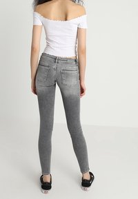 Jeans ajustados grises con un diseño desgastado, dos bolsillos traseros y una cintura alta. Combinados con una blusa blanca de hombros al descubierto y zapatillas negras.