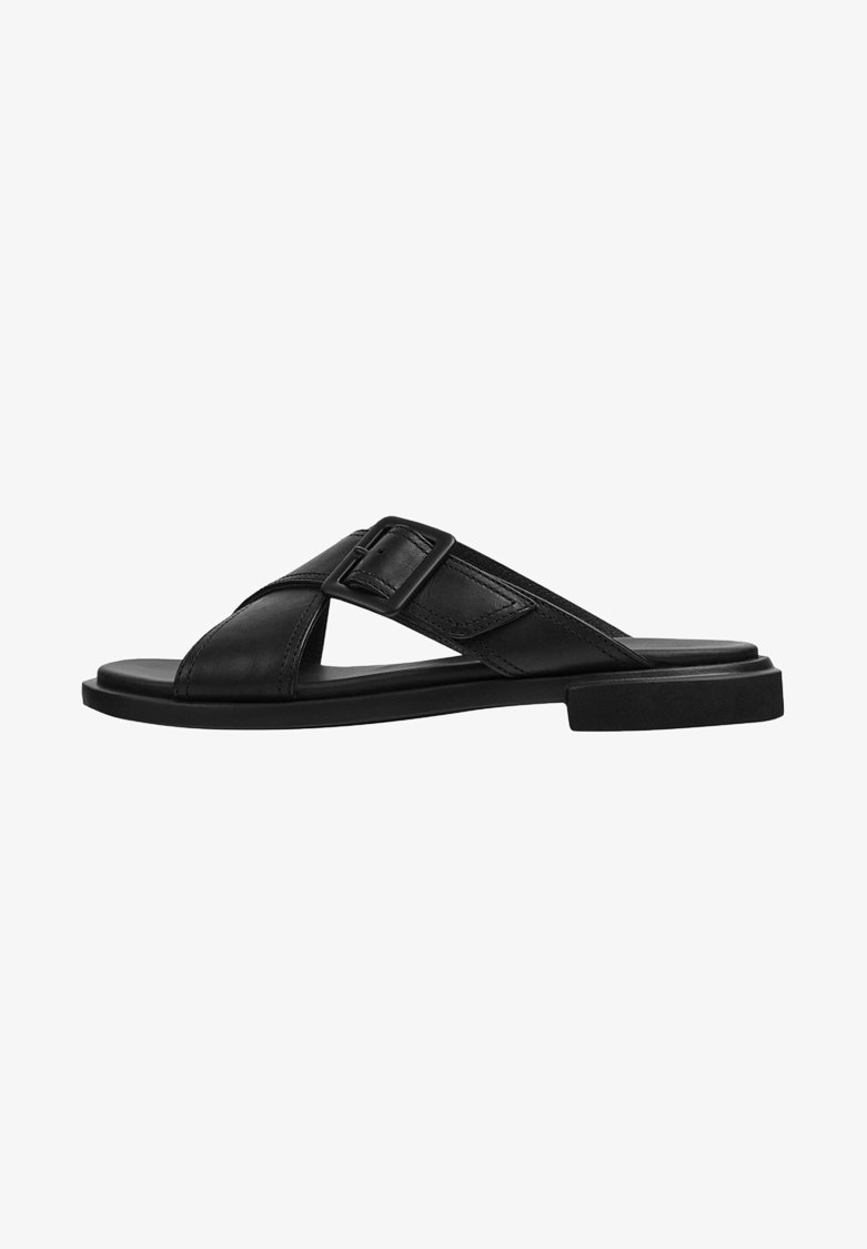 Sandale slide en cuir noir avec des brides croisées et une boucle latérale sur une semelle plate, vue de l'extérieur.