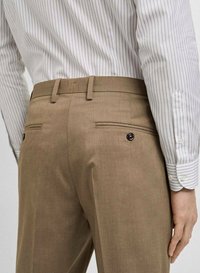 Pantaloni tailored de culoare maro deschis, cu o textură netedă. Au două buzunare posterioare cu accente din butoane. Combinați cu o cămașă albă cu dungi.