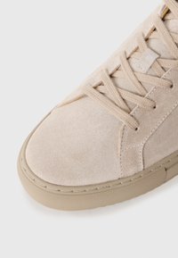 Beige színű bőr sneaker, megfelelõ fűzõvel, lekerekített orral és texturált gumitalppal. Az oldalak mentén található varrások vizuális érdekességet adnak.