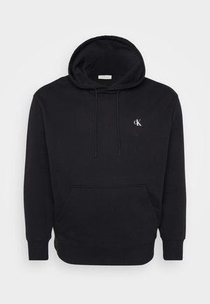 Hoodie noir en tissu doux, avec une poche frontale, un capuchon à cordon de serrage, et un petit logo blanc sur la poitrine.