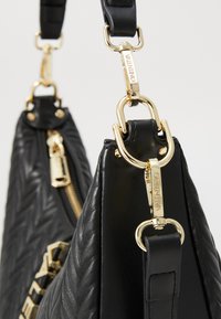 Borsa a tracolla in pelle nera con un design trapuntato, hardware dorato, cerniera e manici removibili. Accentuata da dettagli con logo.