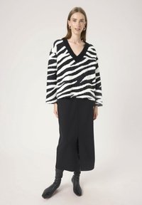 Czarno-biała w paski sweter v-neck o miękkiej, puszystej fakturze, w połączeniu z czarną spódnicą do kolan i czarnymi botkami z ostrym noskiem.