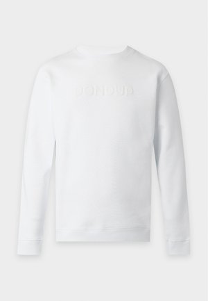 Man wearing a white sweatshirt, loose blue jeans, and black shoes standing with one hand in pocket against a plain white background.