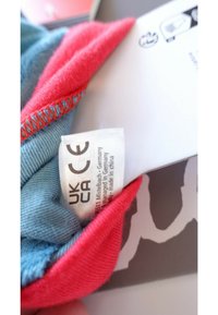 Multicolored fabric with a blue and red blend. Visible tag includes care instructions and country of manufacture. Features stitching detail.