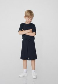 T-shirt noir à manches courtes et short assorti jusqu'aux genoux, associé à des baskets blanches. Tissu lisse avec une coupe décontractée et une taille élastique.