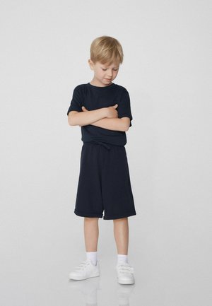 T-shirt noir à manches courtes et short assorti jusqu'aux genoux, associé à des baskets blanches. Tissu lisse avec une coupe décontractée et une taille élastique.