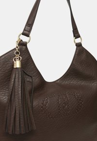 Sac à main en cuir marron foncé avec une surface texturée, motif rond en relief décoratif, attaches en anneau doré et un accessoire en cuir à pampille assorti.
