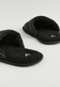 Pantoufles noires à semelle glissante, avec un intérieur texturé et duveteux et un extérieur rembourré. Dotées d'une semelle en caoutchouc et d'un logo sur la semelle intérieure.