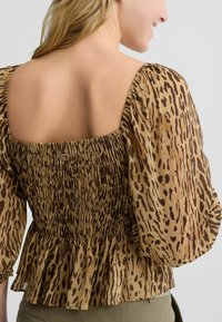 Smešani smeđe i bež top s puf rukavima i uzorkom leopard. Ima smockanu teksturu i volanasti rub. Kvadratni izrez s suptilnim logom.