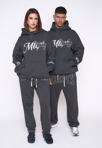 Felpe con cappuccio grigio scuro presentano un grande logo stampato in bianco, abbinate a pantaloni della tuta coordinati. Il materiale sembra morbido con una vestibilità comoda.