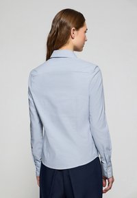 Camicia a maniche lunghe azzurro chiaro con motivo a griglia, polsini abbottonati e colletto classico. Tessuto liscio e vestibilità sartoriale.