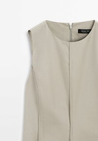 Hihaton, vaaleanharmaa mekko, jossa on pyöreä pääntie ja keskellä vetoketju. Silkkinen kangas, puhtaat saumat ja minimalistinen muotoilu.