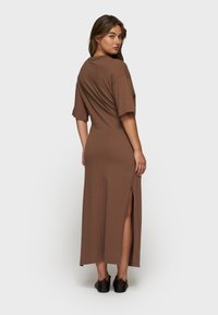 Brązowa sukienka do kostek wykonana z miękkiego materiału. Posiada krótkie rękawy oraz rozcięcie z boku. Casualowy design z luźnym krojem i prostym dekoltem.