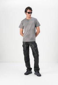 T-shirt de algodão cinza com gola redonda, combinado com calças cargo de couro pretas com bolsos laterais e uma textura suave. Óculos de sol pretos.