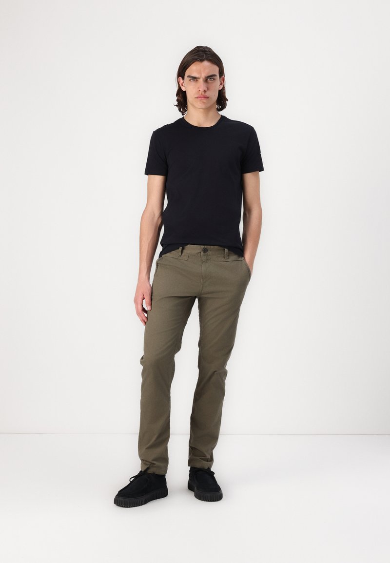 T-shirt noir à manches courtes associé à un pantalon slim-fit khaki et des baskets noires ; tissu lisse, design minimal, couleurs neutres.