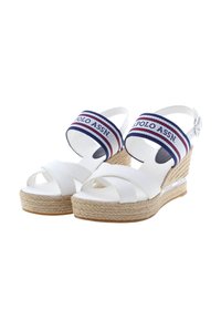 Bílé wedge sandály s překříženými měkkými popruhy, platforma ve stylu espadril vyrobená z juty, a modro-červený textilní pásek s názvem značky.