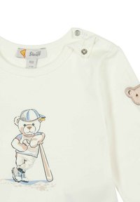 Witte katoenen shirt met een kleurrijke beerafbeelding in sportoutfit, met drukknoopsluiting op de schouder en een geborduurd berenpatch op de mouw.
