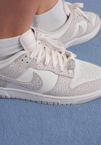 Fehér és szürke mintás Nike sportcipő fehér bokazoknival egy kék szőnyegpadlón.