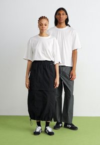 Hvite oversized t-skjorter, svart knelange skjørt, grå bukser og svarte joggesko med hvite striper. Glatt stoff og avslappet passform.